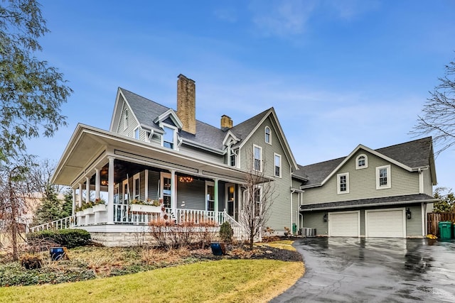 farmhouse featuring a garage, covered porch, a chimney, and aphalt driveway