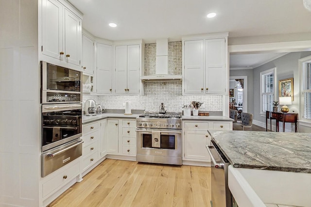 kitchen featuring a warming drawer, appliances with stainless steel finishes, wall chimney range hood, and white cabinetry