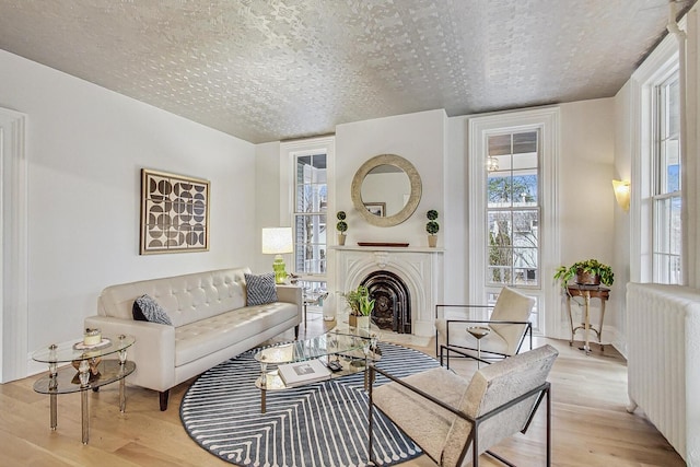 living room featuring a fireplace with flush hearth, a textured ceiling, wood finished floors, and radiator