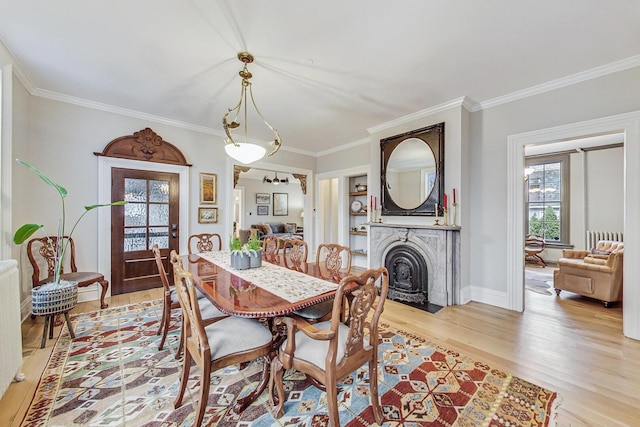 dining space featuring ornamental molding, light wood-type flooring, and a fireplace with flush hearth