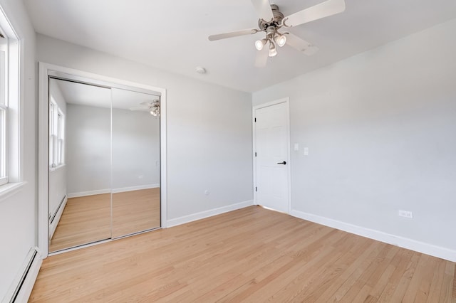 unfurnished bedroom featuring a baseboard heating unit, baseboards, light wood-style flooring, a closet, and a ceiling fan