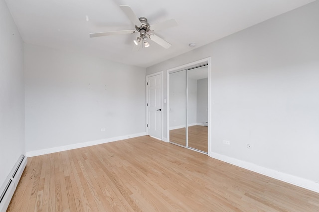 unfurnished bedroom featuring a closet, baseboards, baseboard heating, and light wood-style flooring