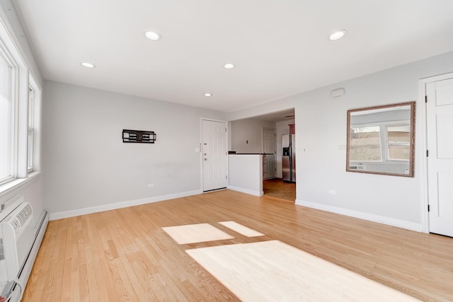 empty room featuring light wood finished floors, baseboard heating, recessed lighting, and baseboards