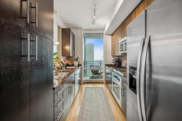 kitchen with track lighting, expansive windows, dark stone counters, appliances with stainless steel finishes, and light wood finished floors