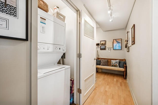 laundry room featuring visible vents, track lighting, stacked washing maching and dryer, light wood finished floors, and laundry area