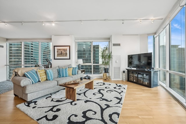 living area featuring a wealth of natural light, visible vents, wood finished floors, and a wall of windows