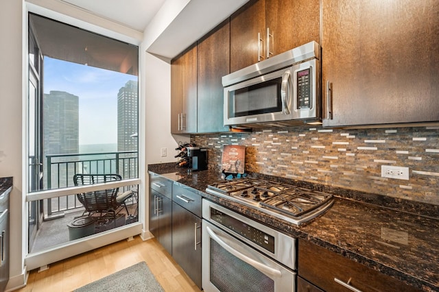 kitchen featuring a city view, dark stone counters, decorative backsplash, appliances with stainless steel finishes, and light wood-style floors