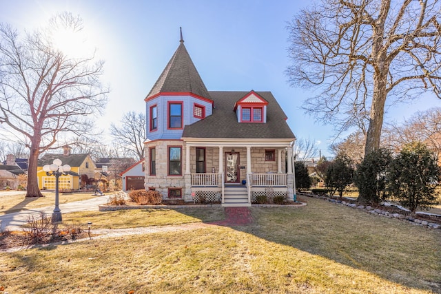 victorian home featuring stone siding, a porch, a front yard, and a shingled roof