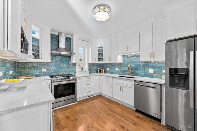 kitchen featuring white cabinets, wall chimney exhaust hood, stainless steel appliances, and a sink