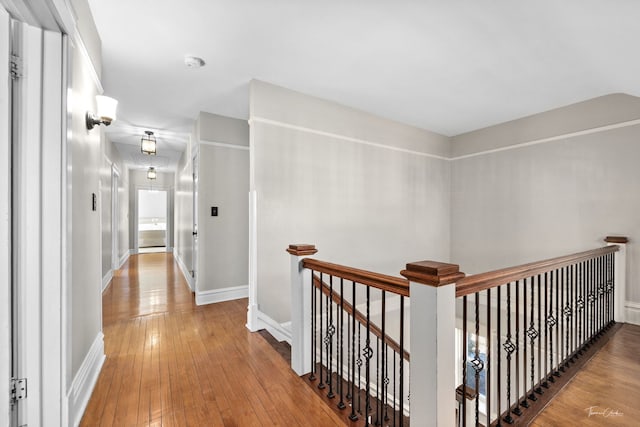 hallway featuring wood-type flooring, baseboards, and an upstairs landing