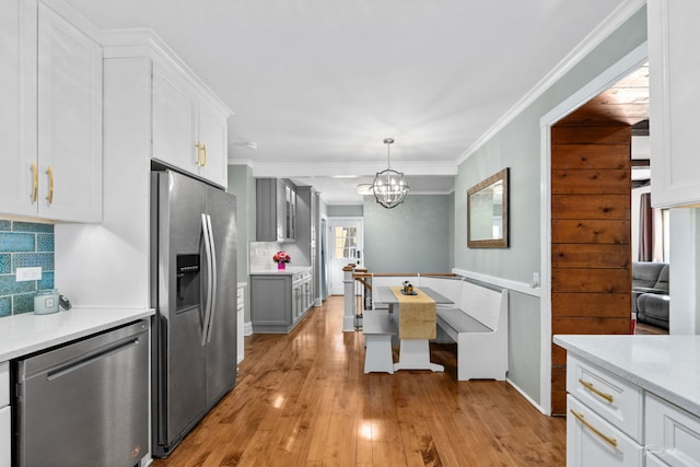 kitchen with light countertops, ornamental molding, appliances with stainless steel finishes, decorative backsplash, and light wood finished floors