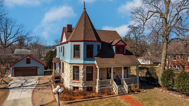 victorian home featuring stone siding, a detached garage, a porch, and an outbuilding