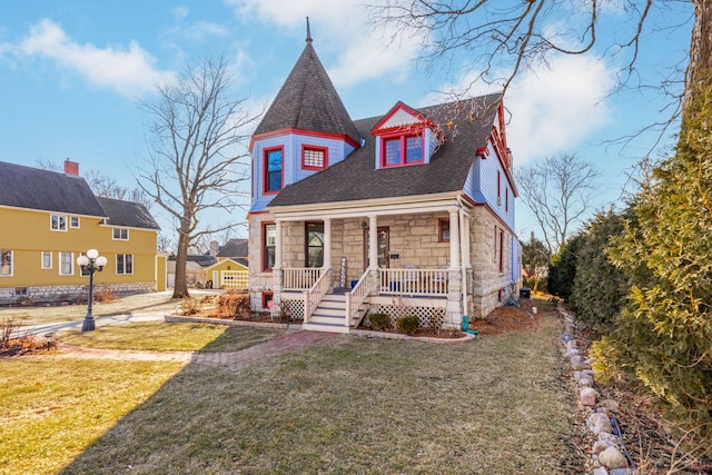 victorian house featuring stone siding, covered porch, roof with shingles, and a front lawn