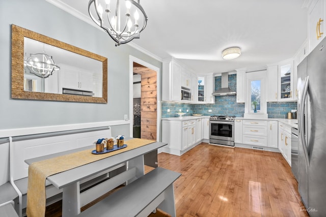 kitchen with decorative backsplash, wall chimney exhaust hood, appliances with stainless steel finishes, crown molding, and a chandelier