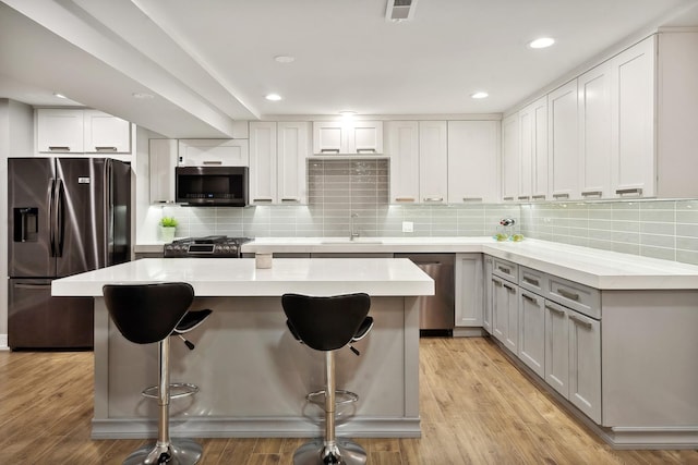 kitchen with light wood-style flooring, stainless steel appliances, a sink, backsplash, and a kitchen bar