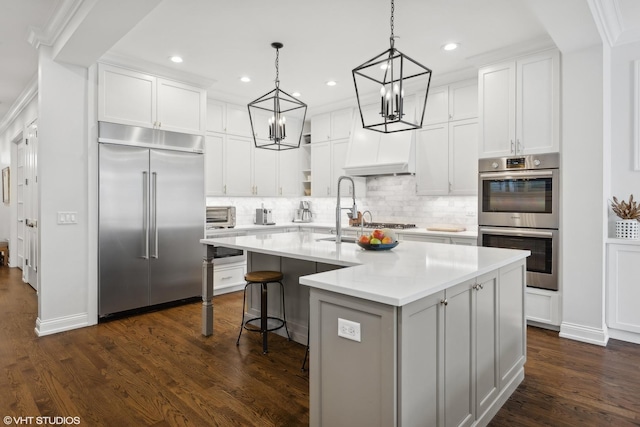 kitchen with a kitchen island with sink, stainless steel appliances, white cabinets, light countertops, and dark wood finished floors