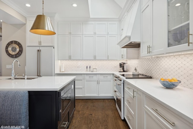 kitchen featuring light countertops, custom range hood, white cabinetry, a sink, and built in appliances