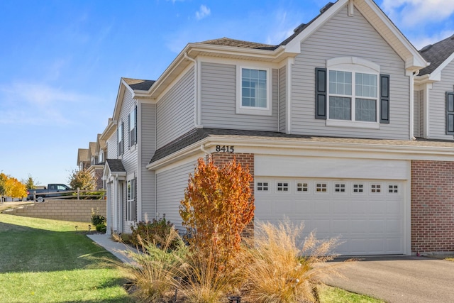 view of side of property featuring a garage, brick siding, driveway, and a lawn