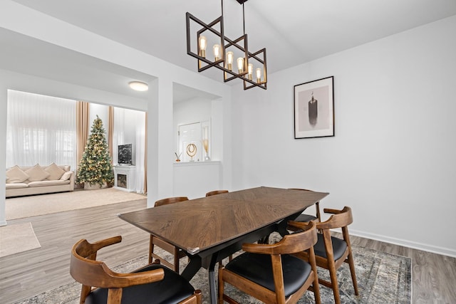 dining room featuring baseboards, a fireplace, a chandelier, and wood finished floors