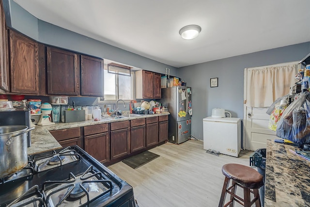 kitchen with freestanding refrigerator, a sink, light wood finished floors, and gas stove