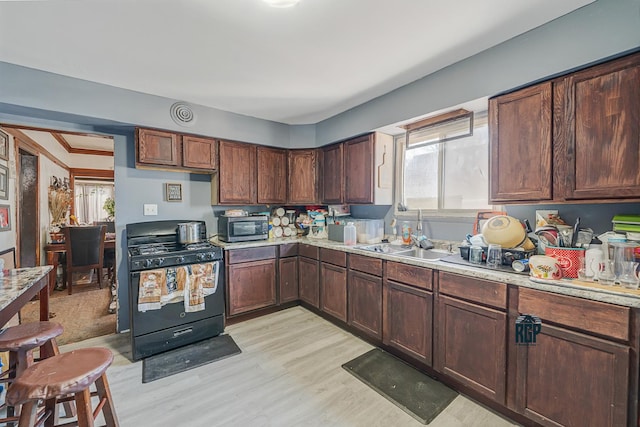 kitchen with black gas range, light wood-style flooring, a sink, light countertops, and stainless steel microwave