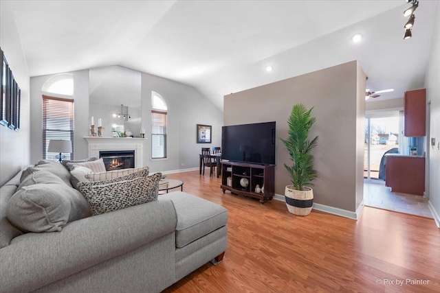 living area with a glass covered fireplace, vaulted ceiling, light wood-style flooring, and baseboards