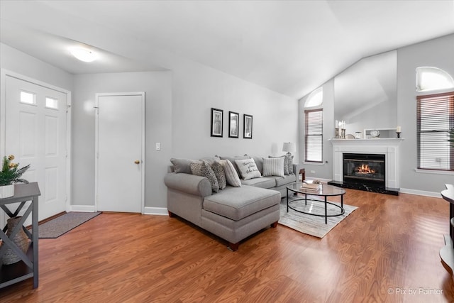 living area featuring vaulted ceiling, a premium fireplace, wood finished floors, and baseboards