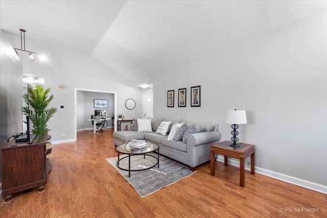 living room featuring high vaulted ceiling, light wood-type flooring, and baseboards