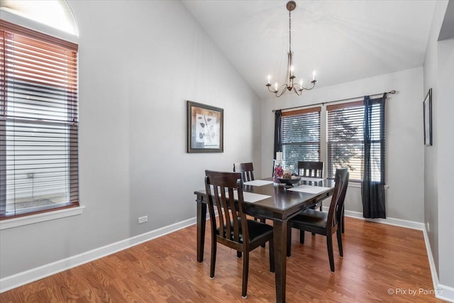 dining room featuring lofted ceiling, wood finished floors, baseboards, and an inviting chandelier