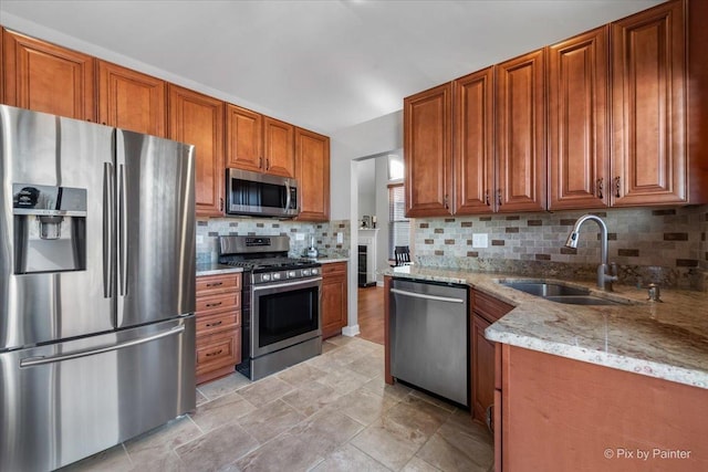 kitchen with light stone counters, stainless steel appliances, a sink, tasteful backsplash, and brown cabinetry