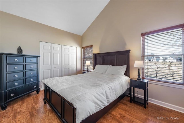 bedroom with a closet, dark wood-style flooring, high vaulted ceiling, and baseboards