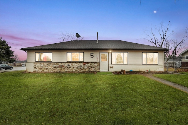 ranch-style home featuring stone siding, a lawn, and fence