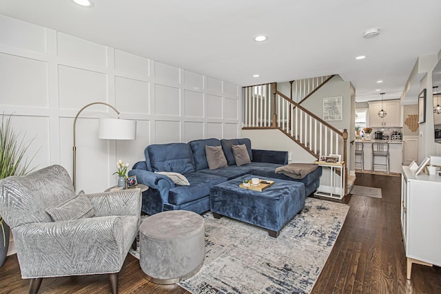 living area featuring recessed lighting, dark wood-style flooring, a decorative wall, and stairs