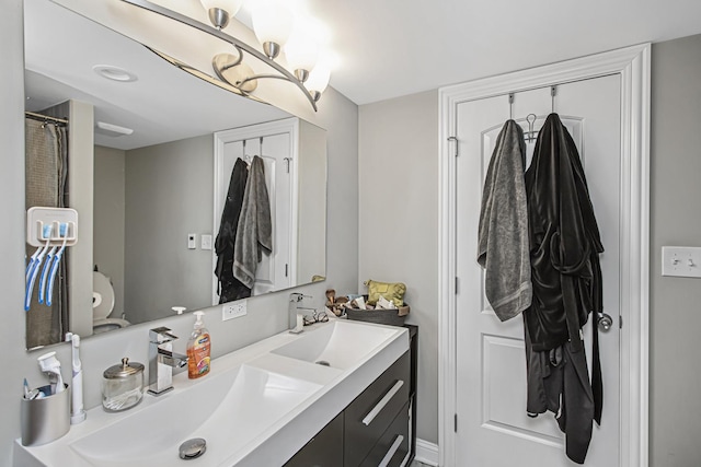 bathroom with double vanity, a sink, toilet, and a notable chandelier