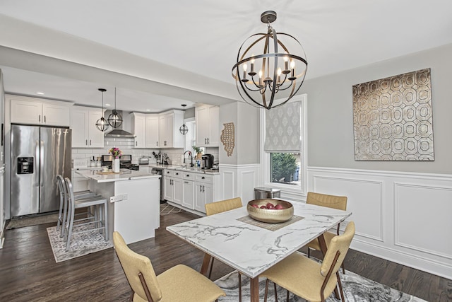 dining room featuring dark wood-style flooring, wainscoting, a notable chandelier, and a decorative wall