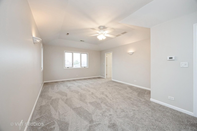 empty room with ceiling fan, a raised ceiling, light colored carpet, and baseboards