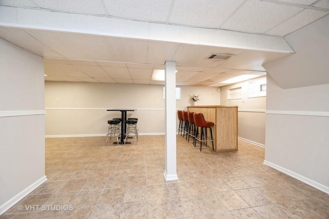 below grade area with visible vents, light tile patterned floors, baseboards, a dry bar, and a drop ceiling