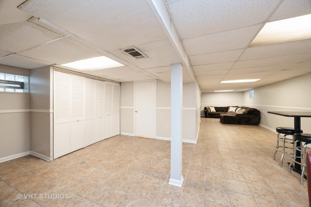basement with a paneled ceiling, baseboards, and visible vents