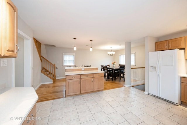 kitchen with light countertops, white refrigerator with ice dispenser, hanging light fixtures, and a wealth of natural light