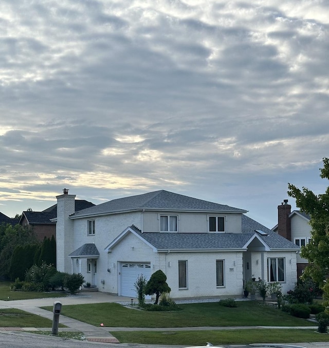 traditional home featuring driveway, a shingled roof, a chimney, an attached garage, and a yard