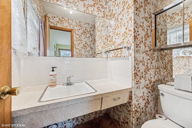 half bathroom featuring a sink, toilet, a healthy amount of sunlight, and wallpapered walls