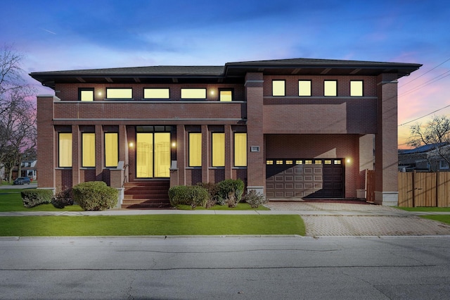 prairie-style house featuring a garage, decorative driveway, brick siding, and fence