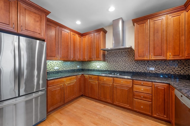 kitchen featuring light wood finished floors, stainless steel appliances, wall chimney range hood, and brown cabinetry