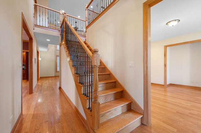 stairs with a towering ceiling, baseboards, and wood finished floors