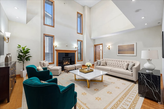 living room with a towering ceiling, a glass covered fireplace, light wood-style flooring, and recessed lighting