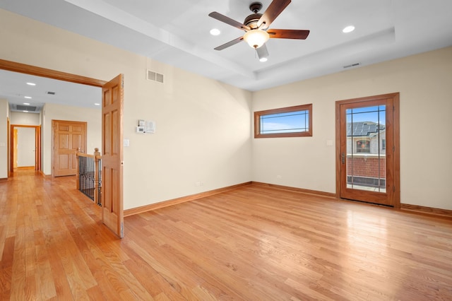 empty room with light wood-style flooring, a raised ceiling, visible vents, and baseboards