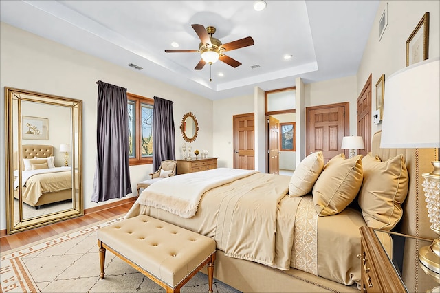 bedroom with a tray ceiling, recessed lighting, visible vents, a ceiling fan, and light wood-type flooring