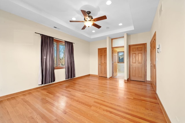 unfurnished bedroom with a tray ceiling, light wood-style flooring, visible vents, and baseboards