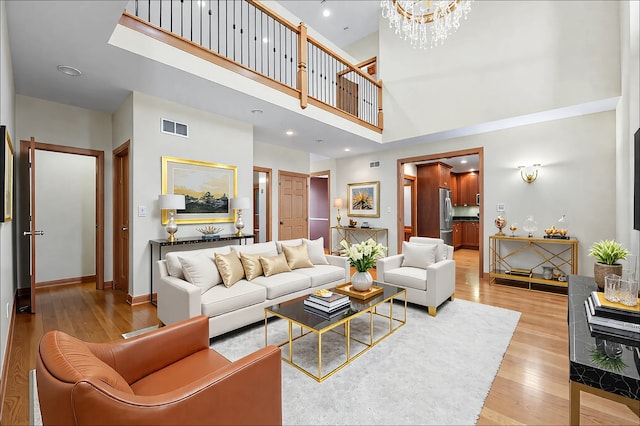 living room featuring a notable chandelier, visible vents, a high ceiling, light wood-style floors, and baseboards