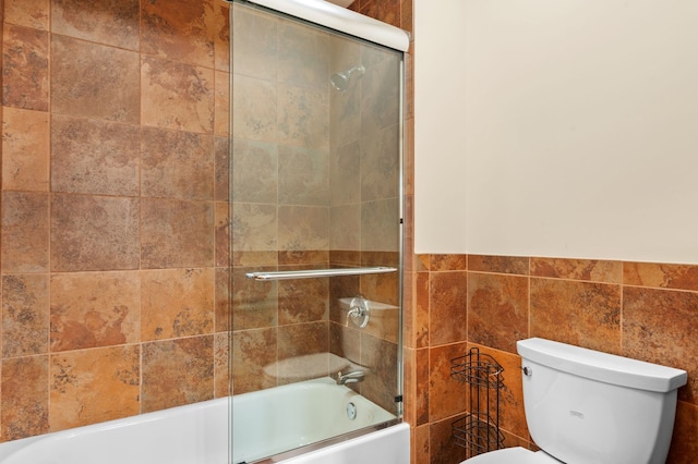 full bathroom featuring bath / shower combo with glass door, toilet, and tile walls